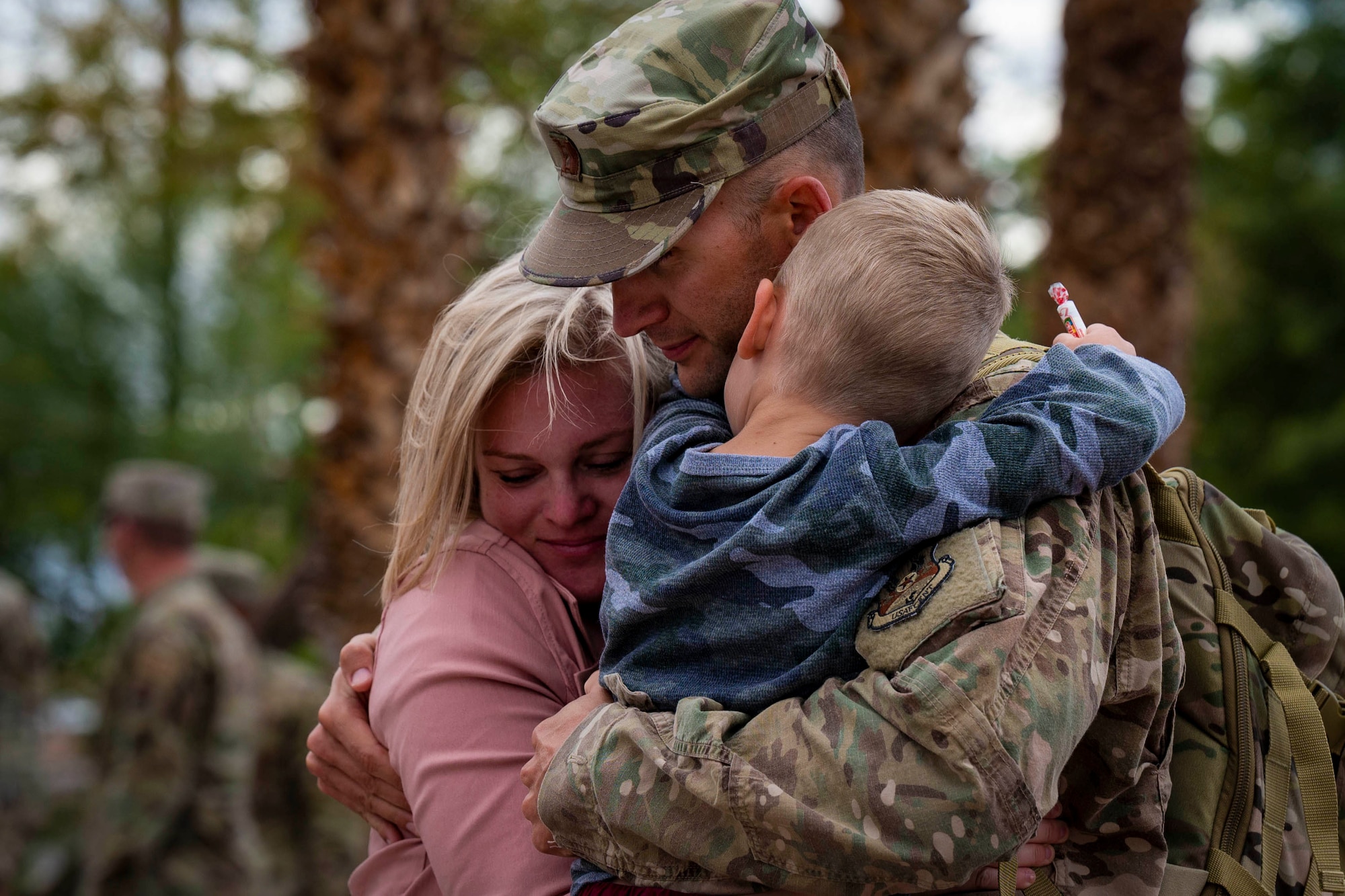 A soldier hugs a child and a woman.