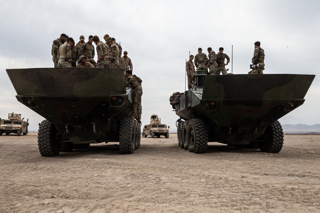 Marines stand on top of two large vehicles.