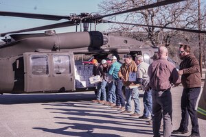 People stand in a line outside a helicopter passing boxes down an assembly line.