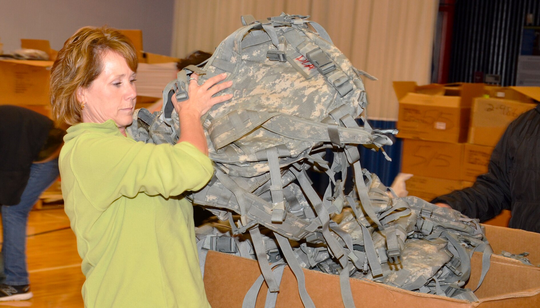 Woman in a green shirt pulls backpacks out of a box.