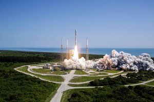 Smoke plumes around rockets getting ready to launch on a green pad close to the ocean.