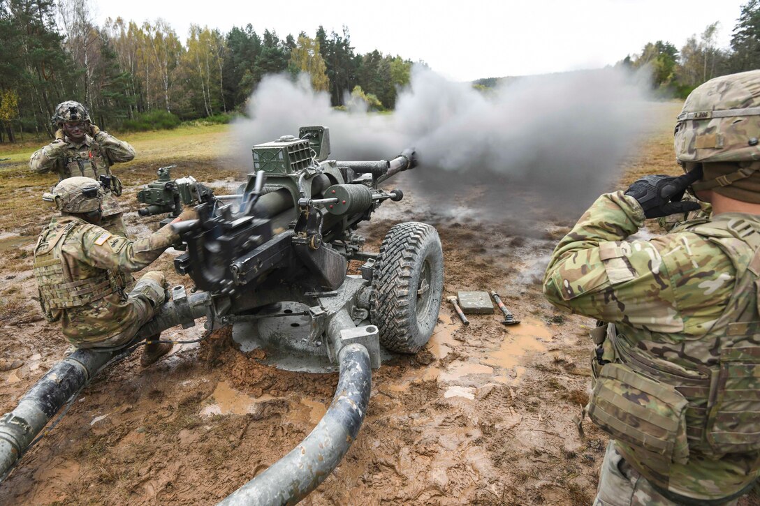 Soldiers fire a tank in a field.