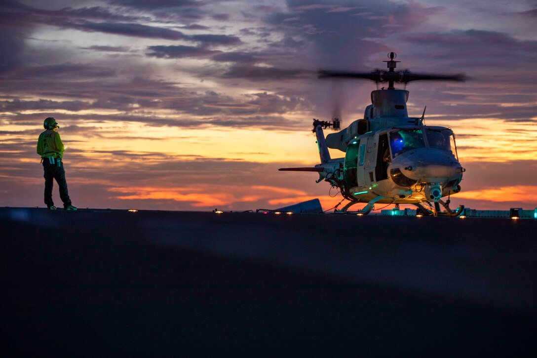 A sailor stands next to a parked helicopter.