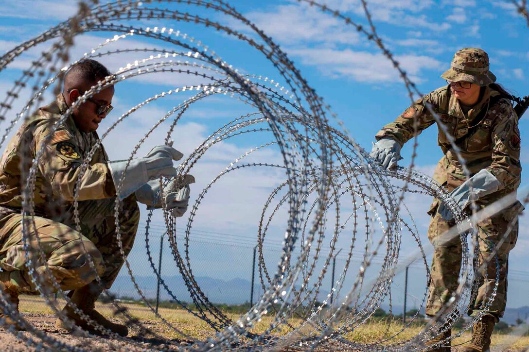 Two airmen set up barbed wire fencing.