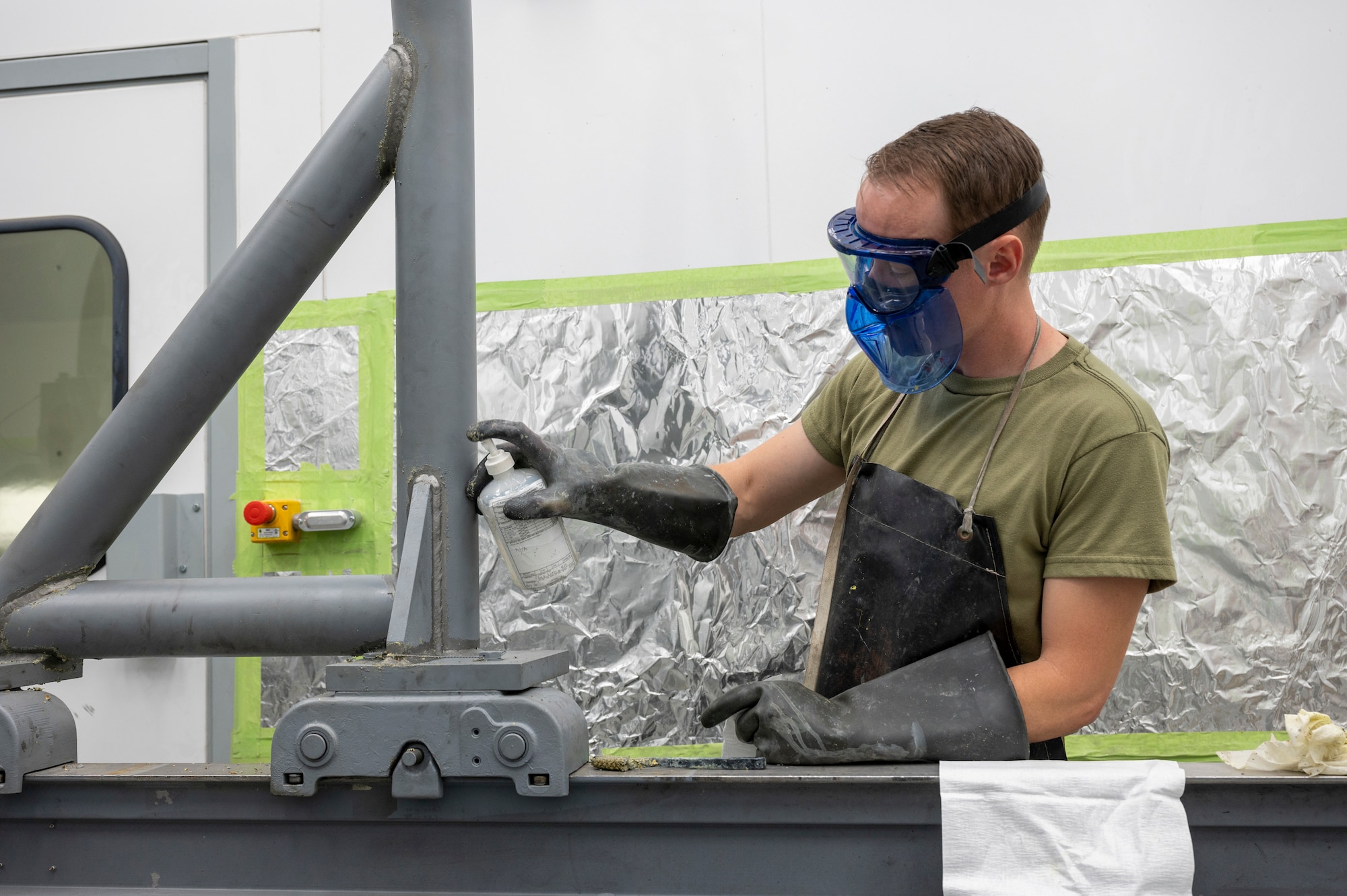 Amn Henry Crabtree sprays paint stripper onto a metal surface.