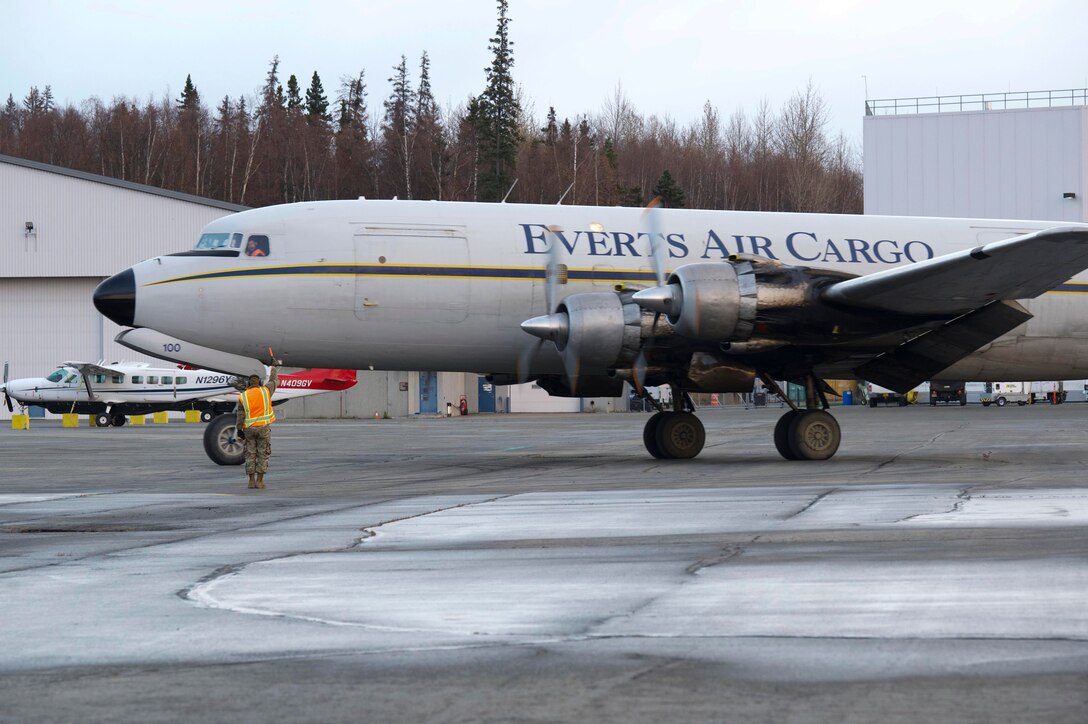 Air Force Staff Sgt. Anthony Mahon, 732nd Air Mobility Squadron, signals a Douglas DC-6 pilot to hold short prior to departure during the Nodal Lightning at Ted Steven International Airport in Anchorage, Alaska, Oct. 19, 2021. he Nodal Lightning exercise allowed the 732nd AMS personnel to respond efficiently and effectively to contested or degraded contingency environments.