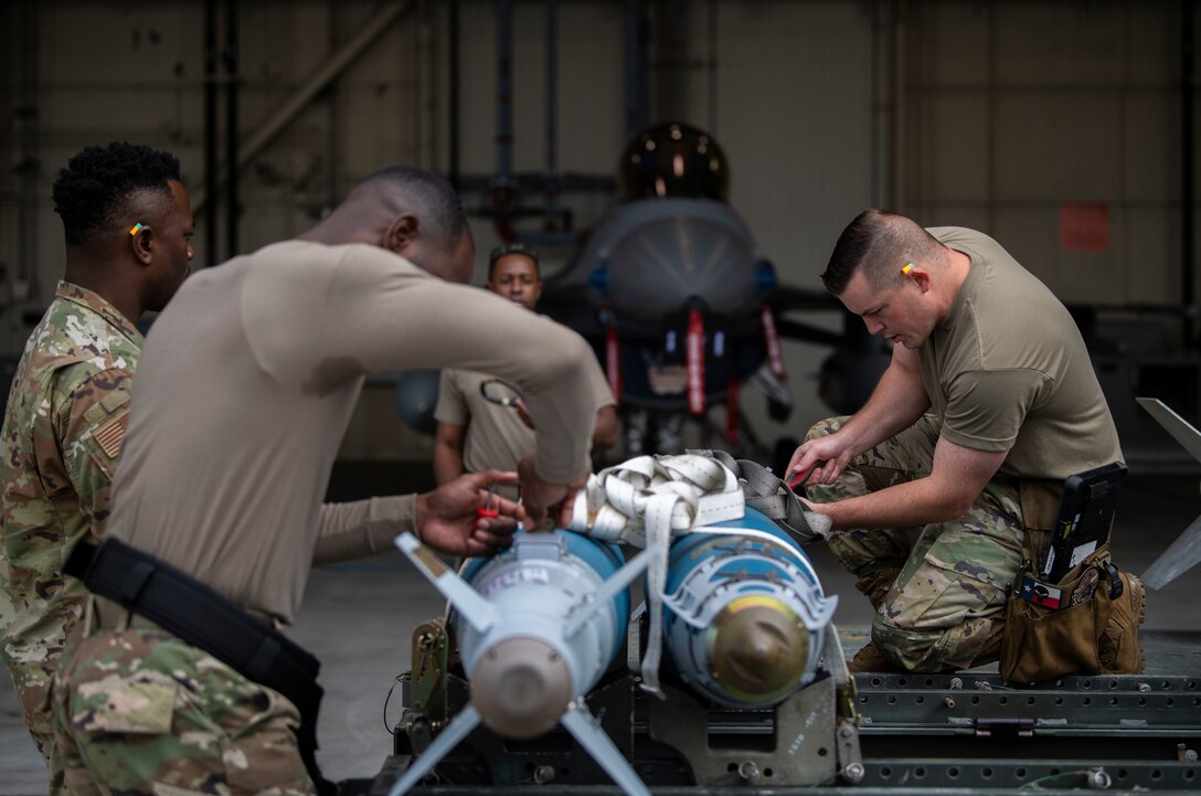 Weapons load crew team members assigned to the 35th Aircraft Maintenance Unit unstrap munitions during the Third Quarter Load Crew Competition at Kunsan Air Base, Republic of Korea, Oct. 16, 2021. Three teams competed in four categories to include dress and appearance, a weapons knowledge test, a toolbox inspection and a weapons load. (U.S. Air Force photo by Senior Airman Suzie Plotnikov)