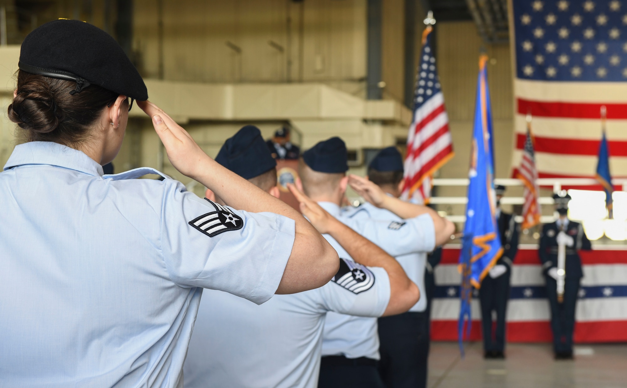 Airmen stand at attention and salute while facing the stage.