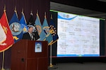 Sub-command director stands at a podium and speaks about topics included on a slide show presentation.