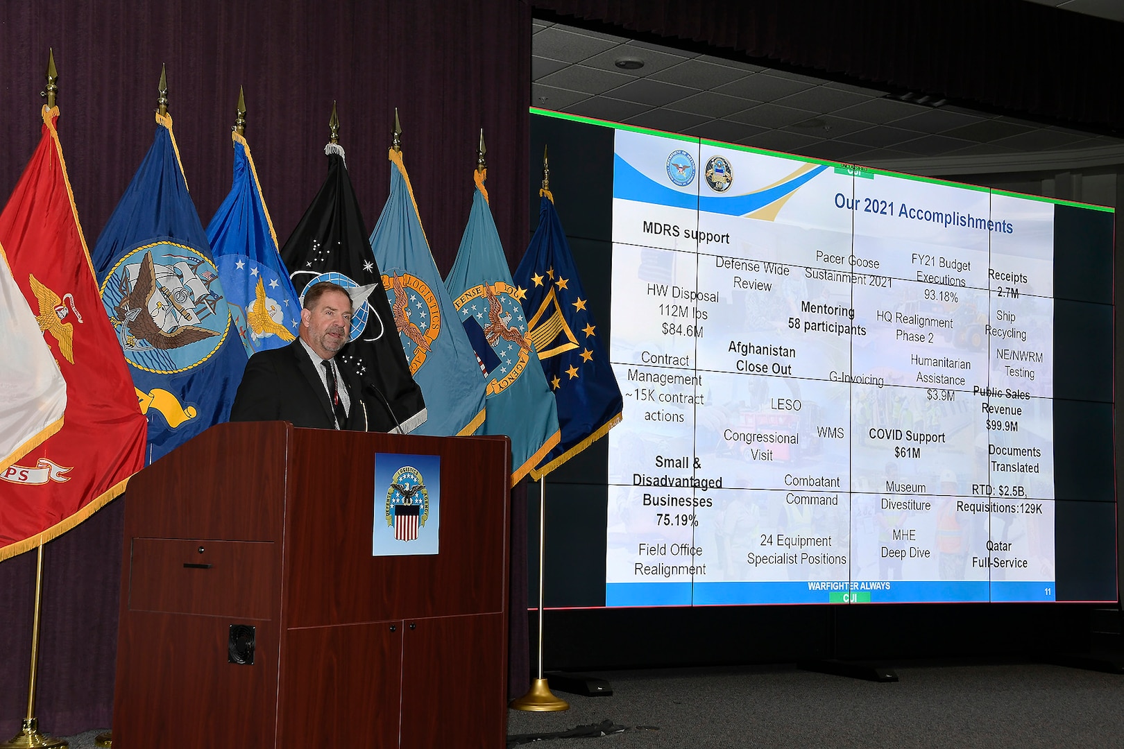 Sub-command director stands at a podium and speaks about topics included on a slide show presentation.