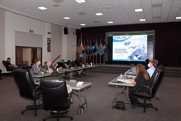 Socially distanced leaders sit at tables listening to a presentation