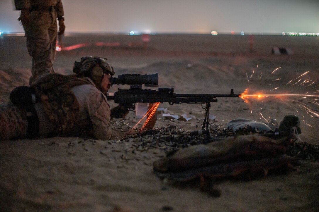 A sailor lies on the ground and fires a machine gun.