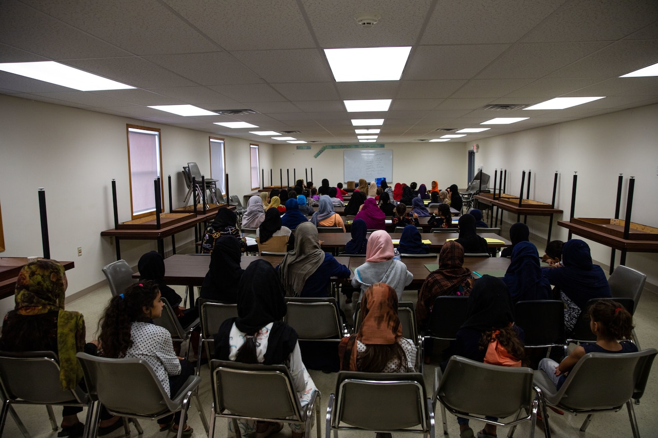 A large group of people sit with their backs to the camera in a large room.