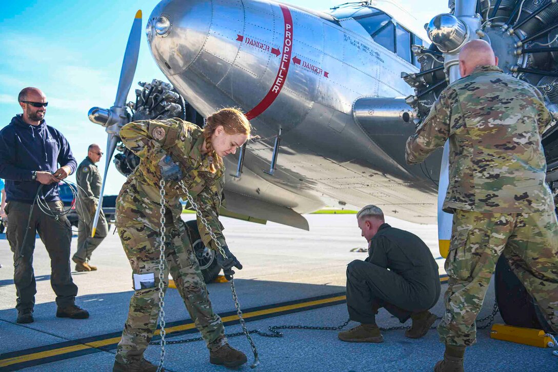 Airmen pull a chain attached to an aircraft as others stand around.