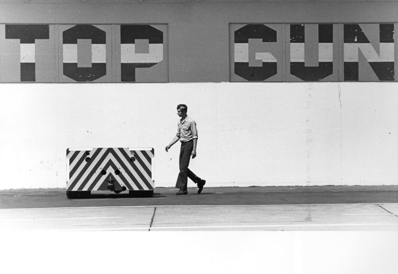 A man walks past the side of a building with a large logo that says "TOPGUN."