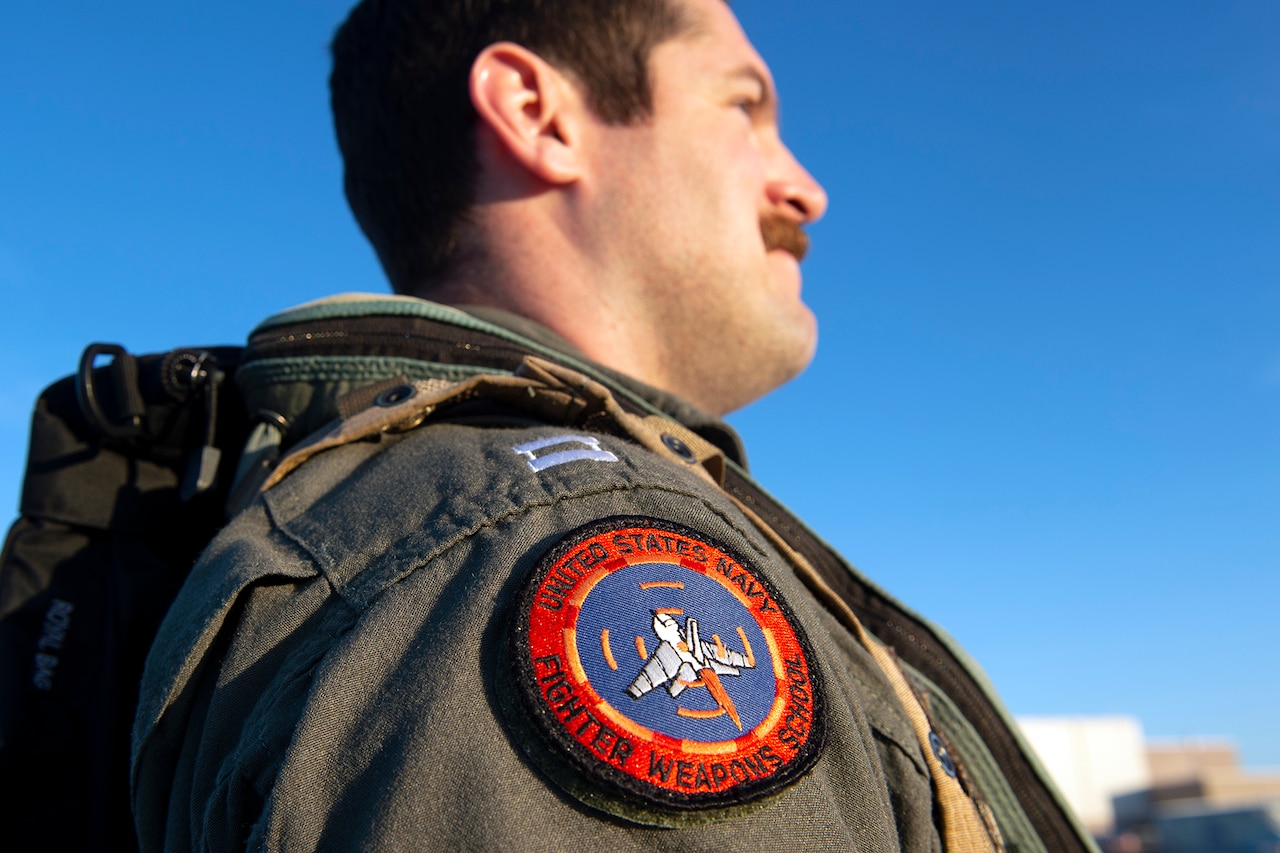 A circular red patch is attached to a man's right shoulder sleeve.