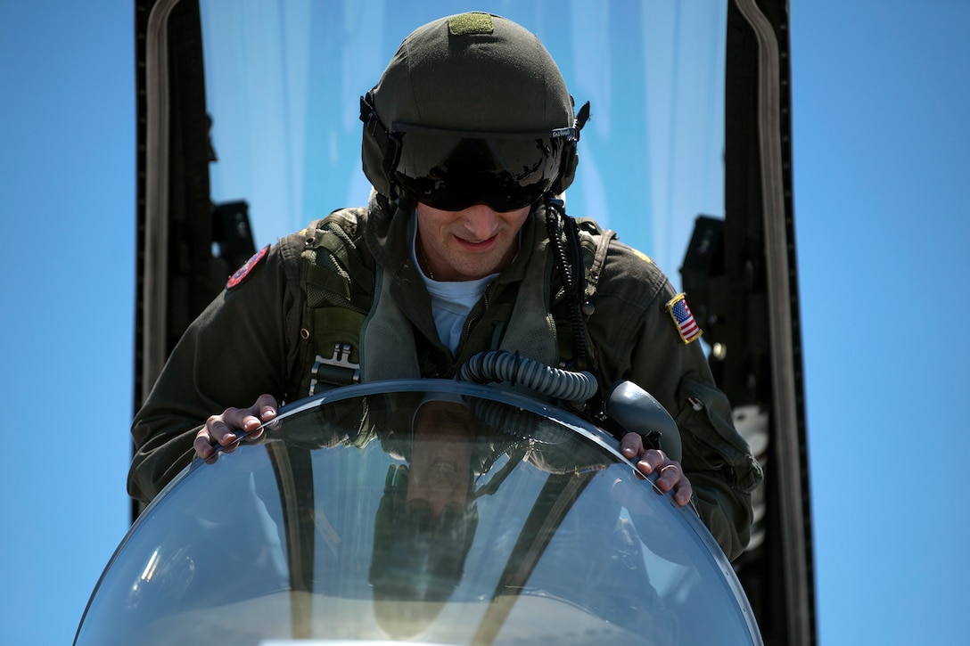 A pilot in a helmet climbs into the cockpit of a fighter jet.
