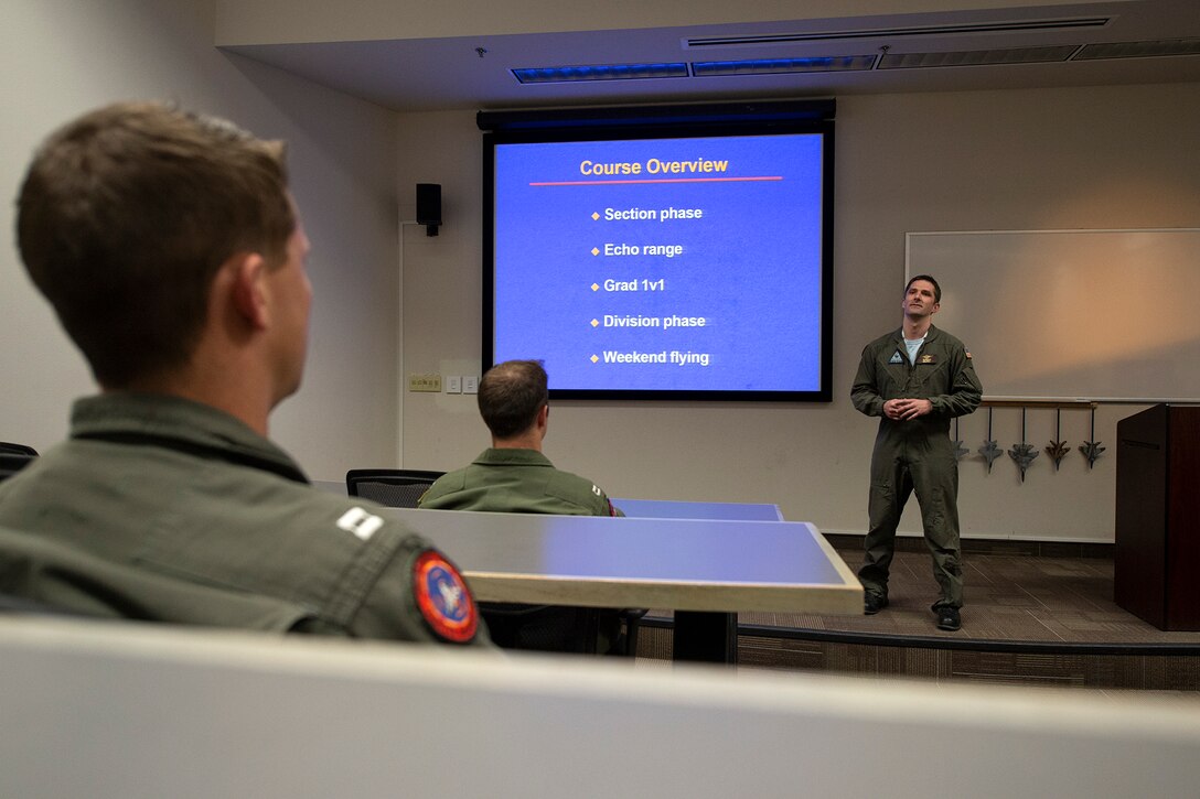 An instructor stands in front of a screen that two students look at.