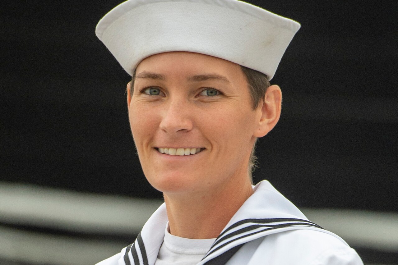 A sailor in dress whites smiles for a photo.