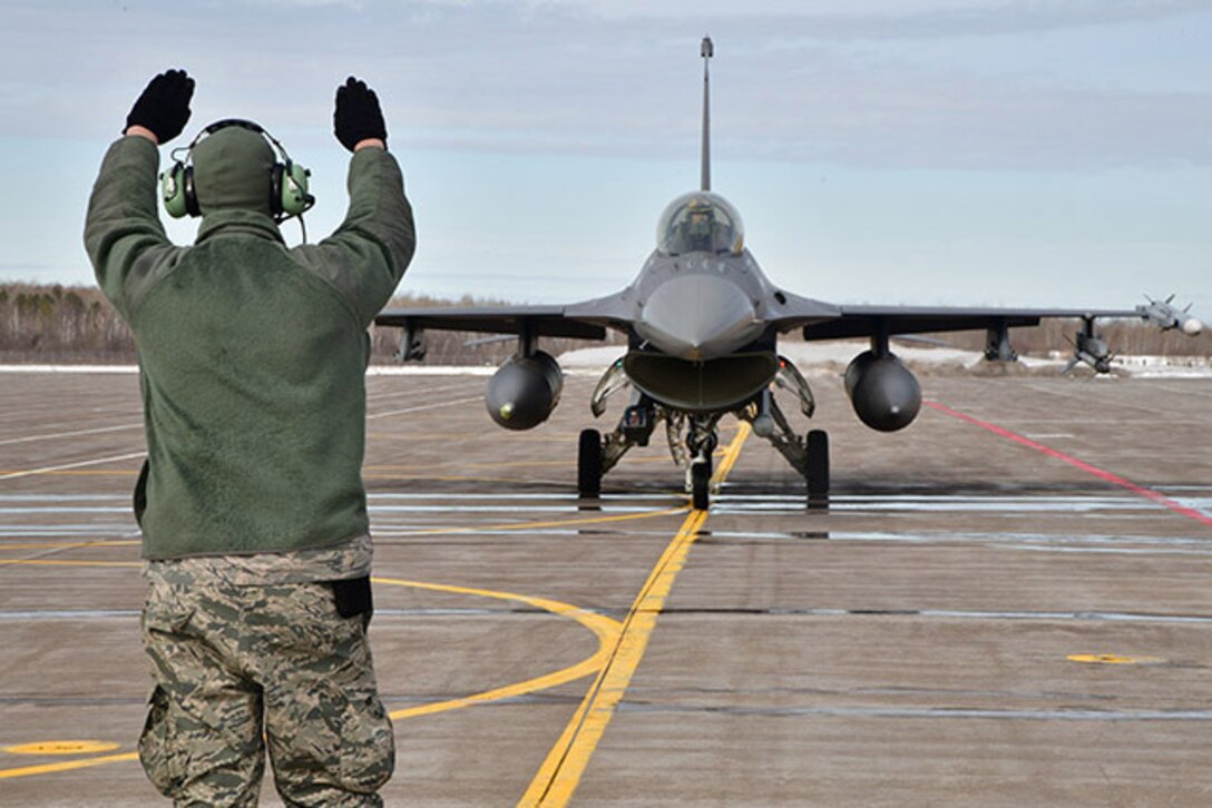 A service member directs a plane on a runway.