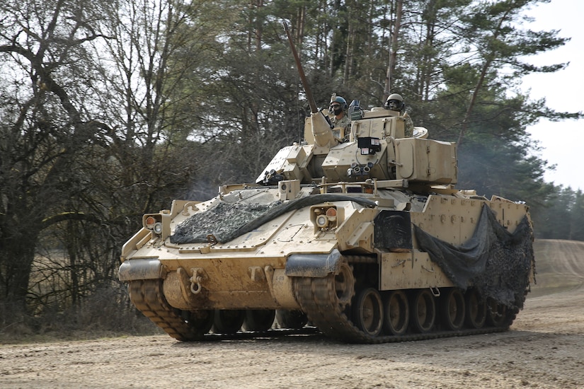 A tank rolls down a dirt road.