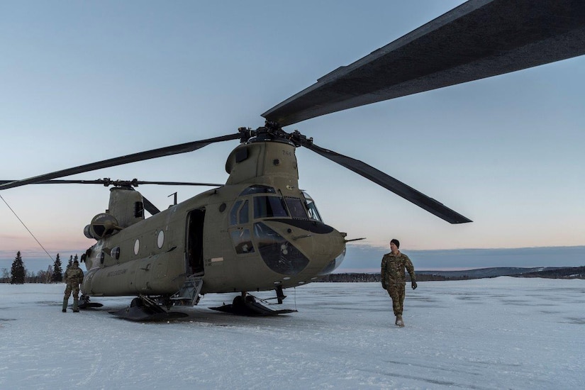 Two service members walk around a large helicopter.