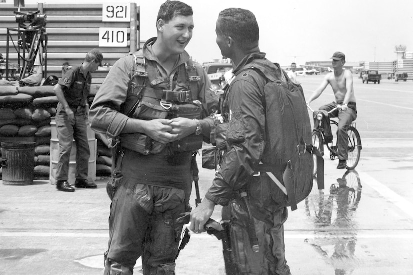 Two men in pilot uniforms greet one another.
