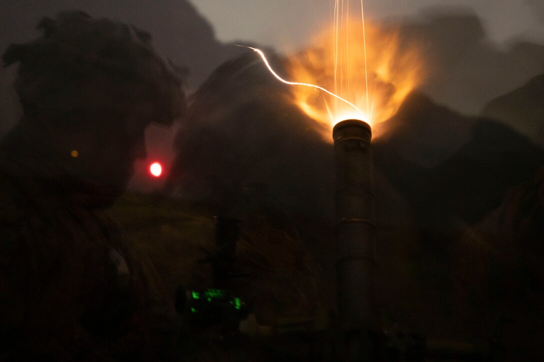 Marines fire a weapon in the dark illuminated by colorful lights.