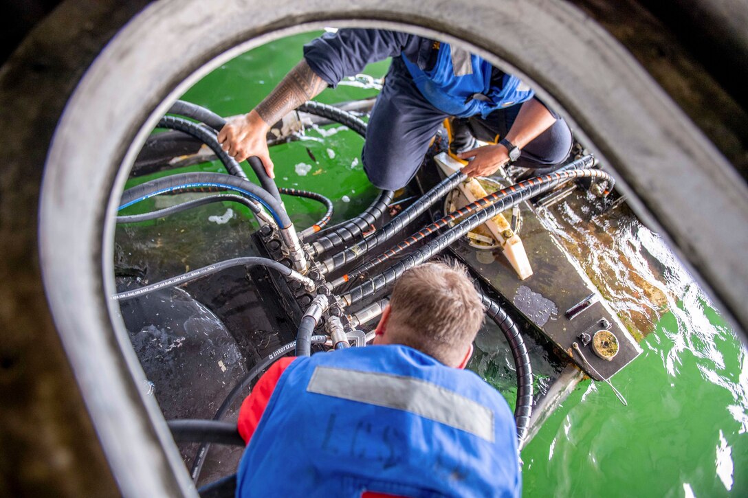 Sailors perform maintenance on a water jet as seen from above.