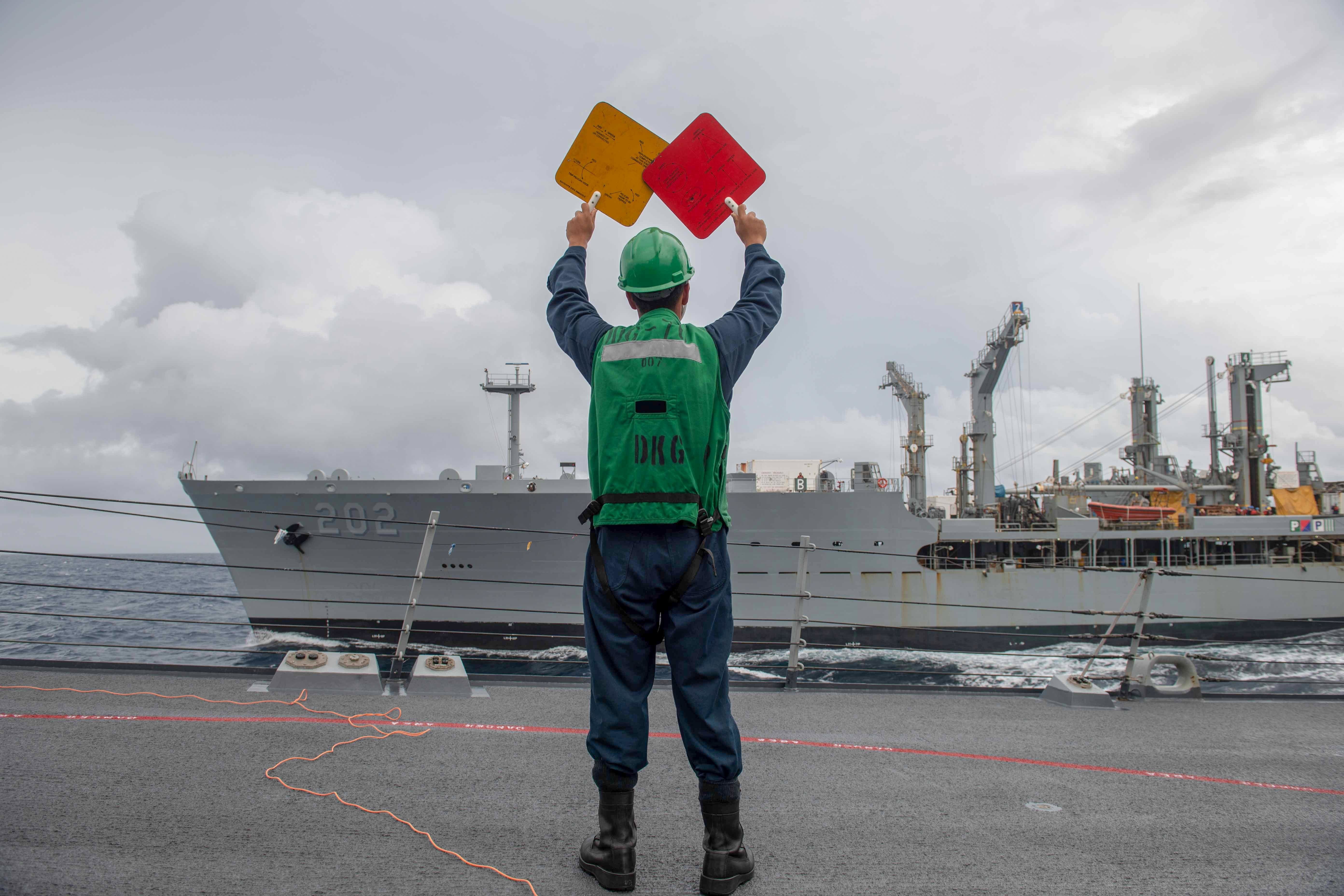 Seaman Nabeel Adam signals to Henry J. Kaiser-class oiler USNS Yukon (T-AO 202)  during a replenishment at sea aboard Arleigh Burke-class guided-missile destroyer USS Higgins (DDG 76).