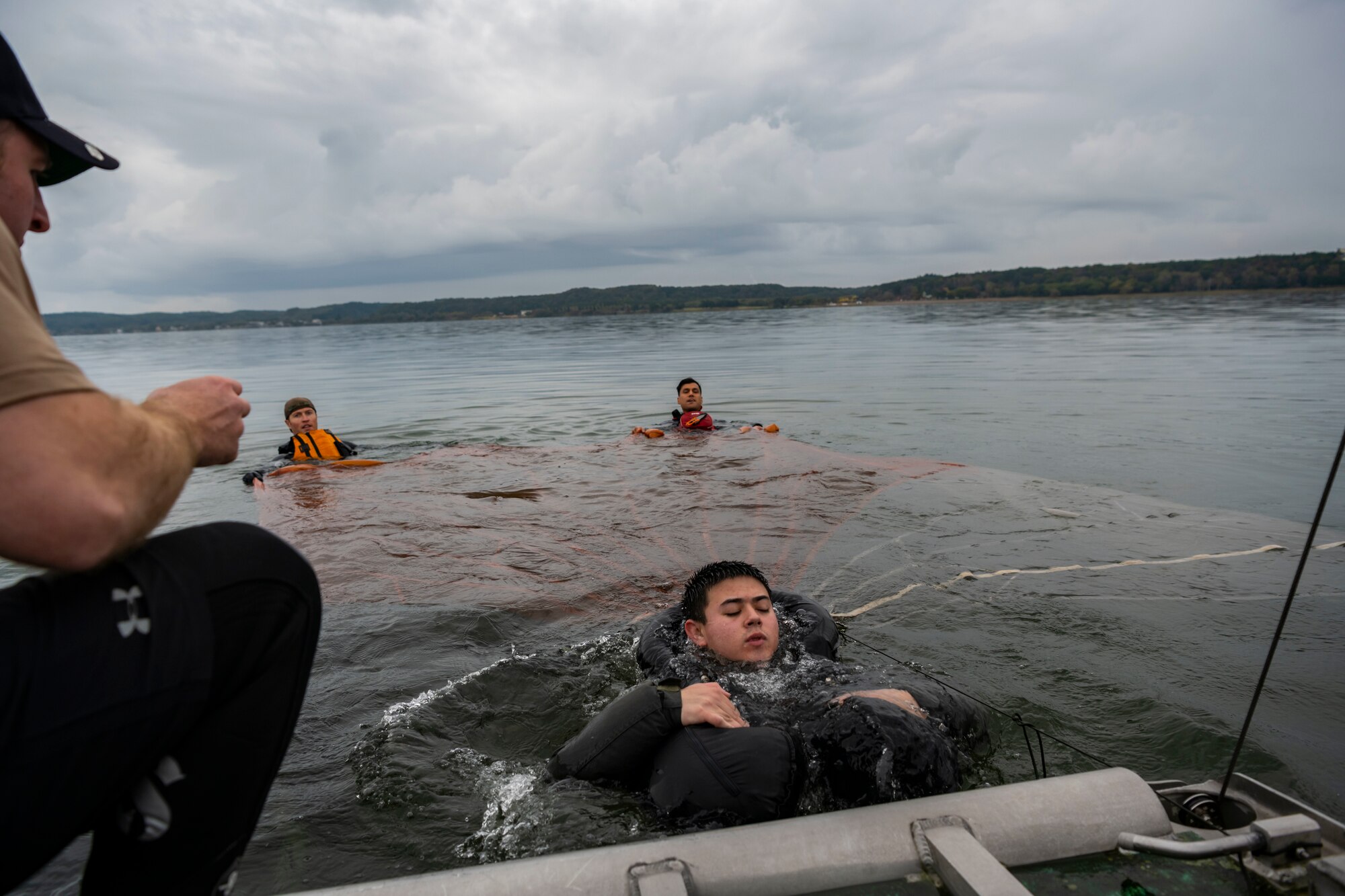 Military members swim in the water holding a parachute canopy open.