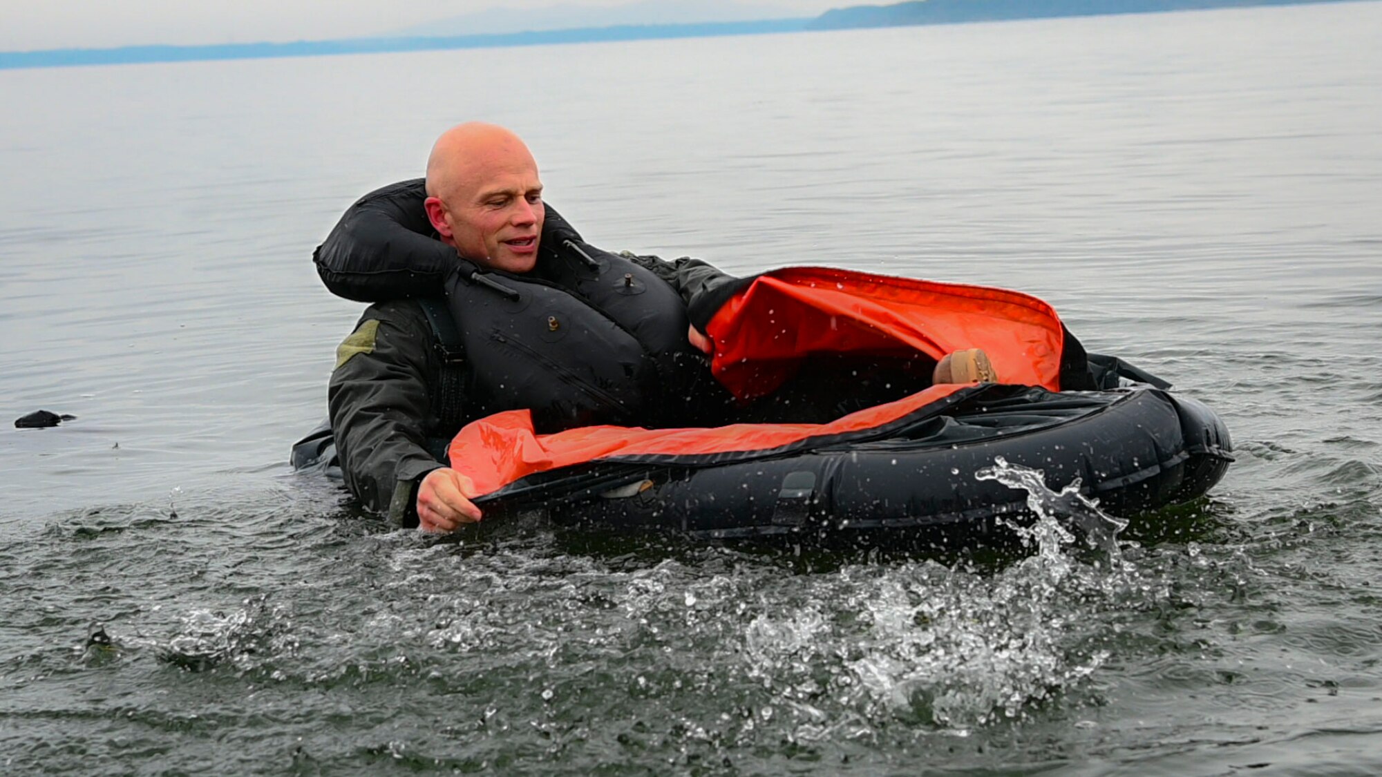 Military member removes water while sitting in a life raft.