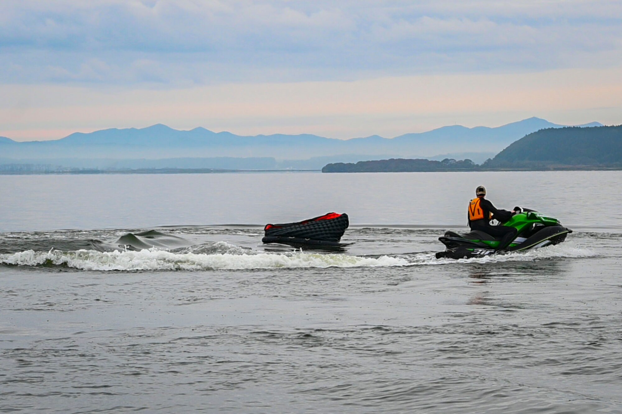 Military member rides a jet ski around a life raft in the water.