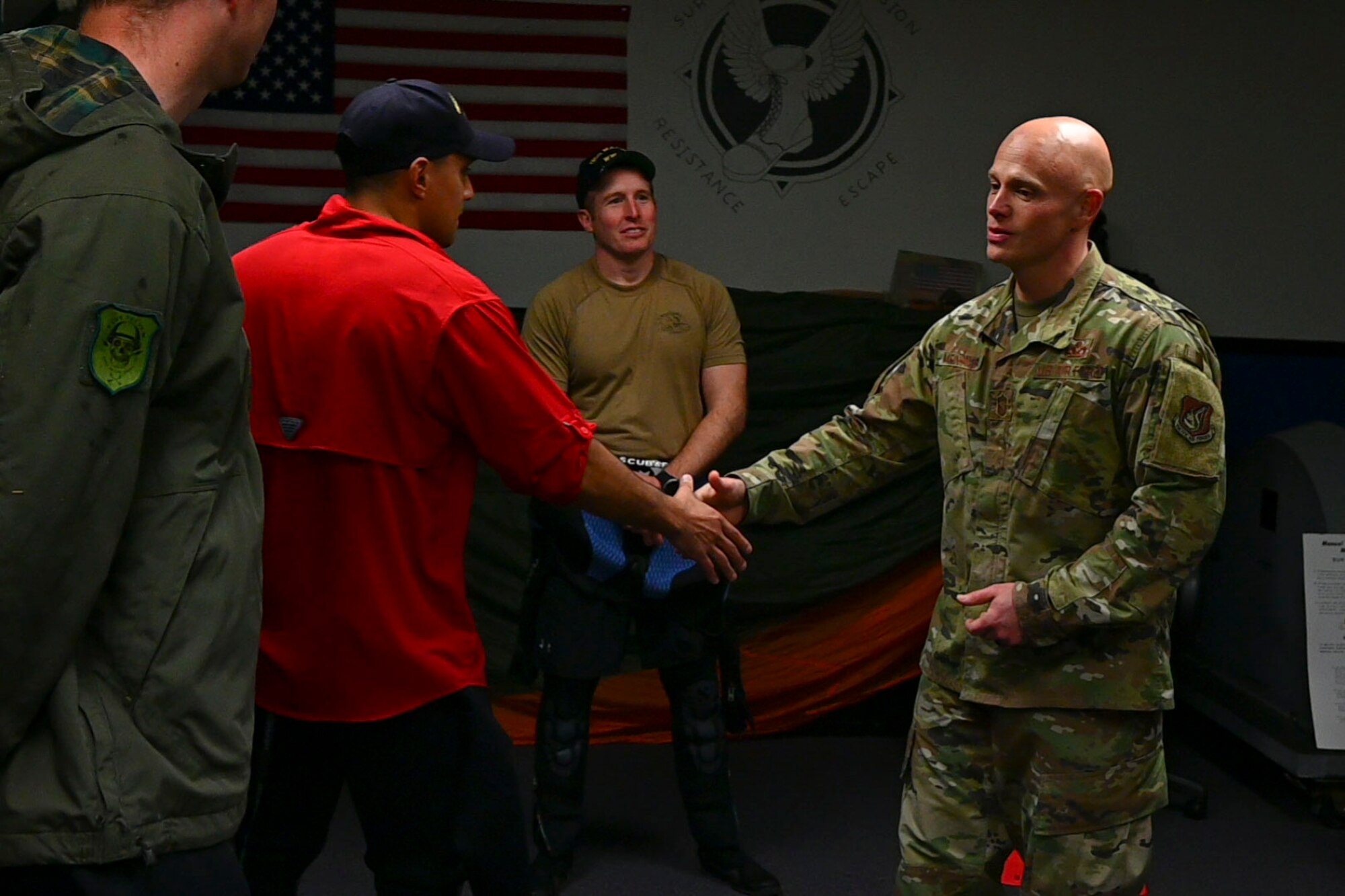 Military member in uniform shakes hands with three other military members.