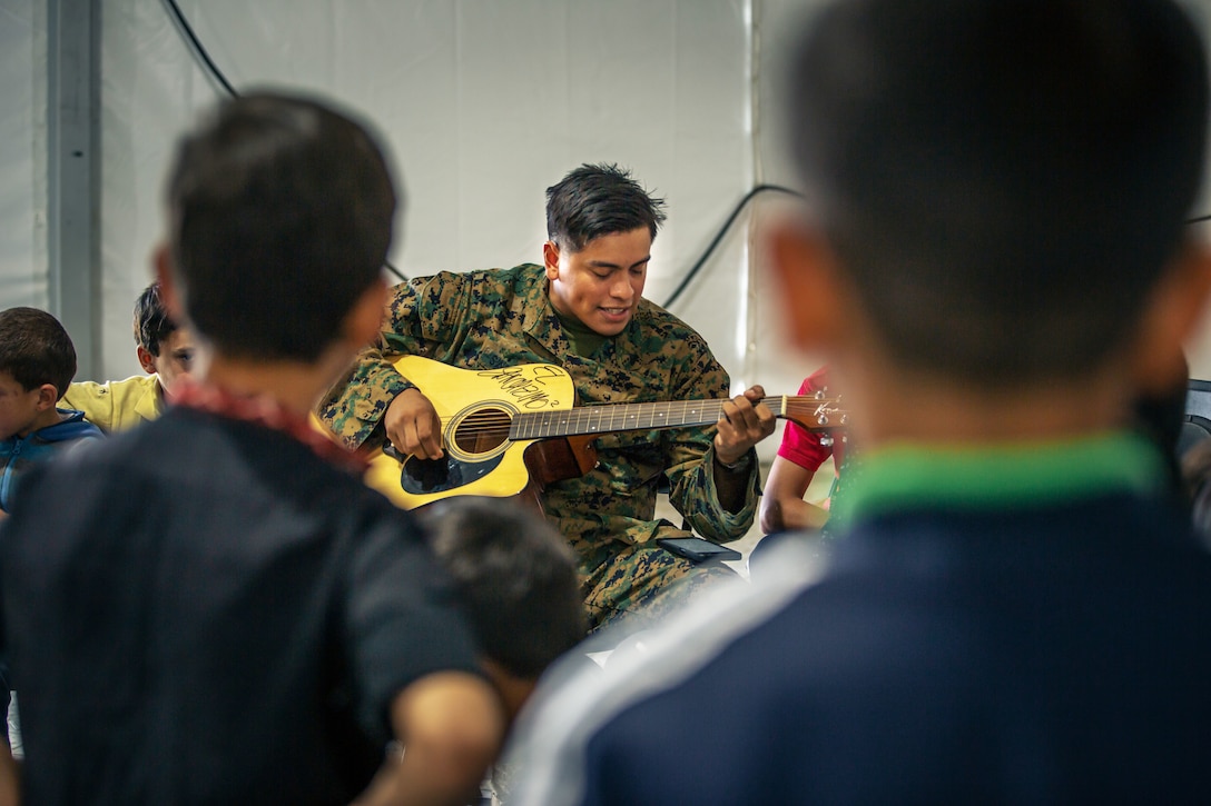 A soldier plays the guitar to entertain Afghanistan children