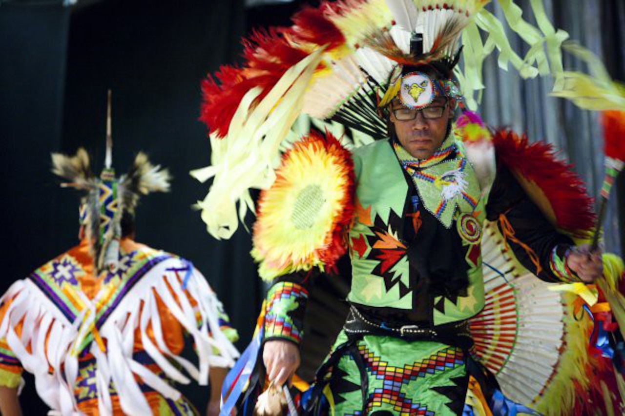 A Native American man dances. Another man dances in the background.