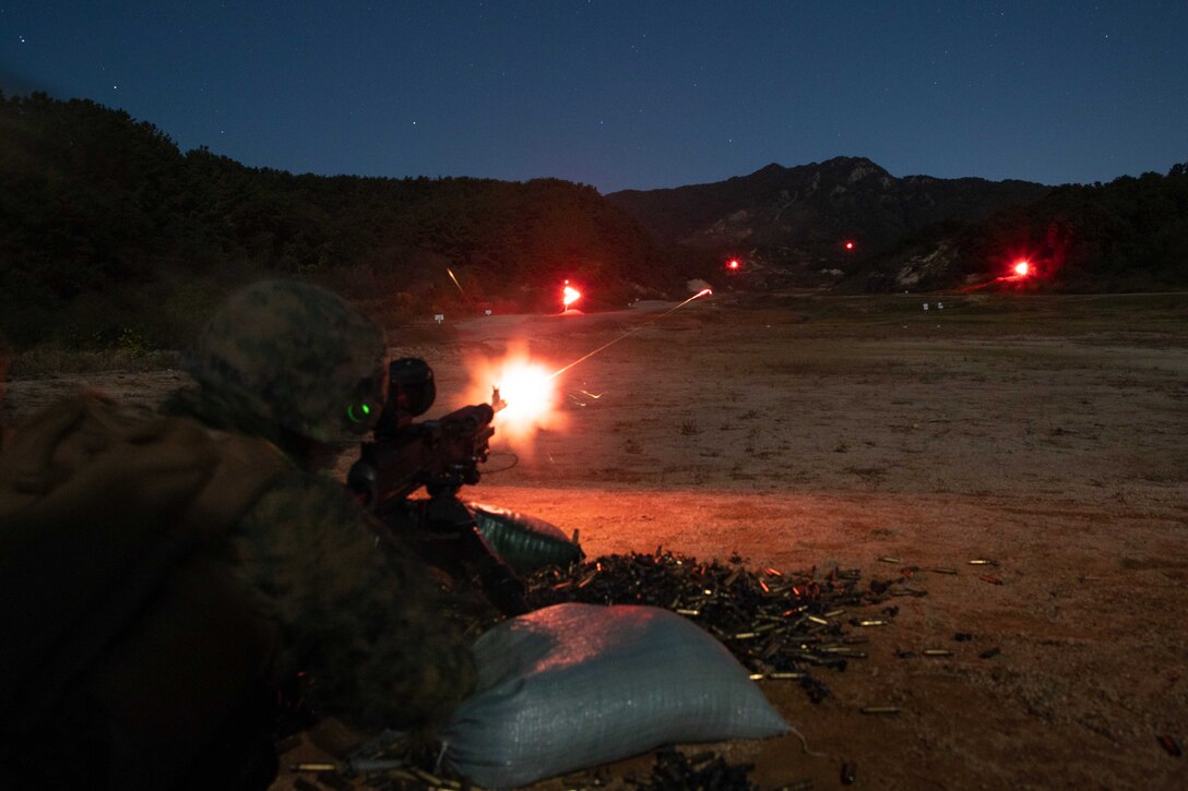 Marines create bursts of fire at night while firing at targets from a crouched position.
