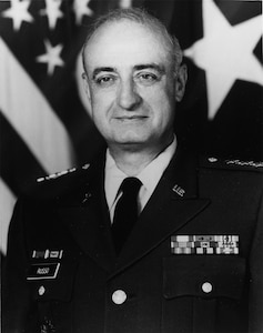 Male Army Lieutenant General in front of flags.