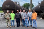 a group of people stand in front of fuel rail cars