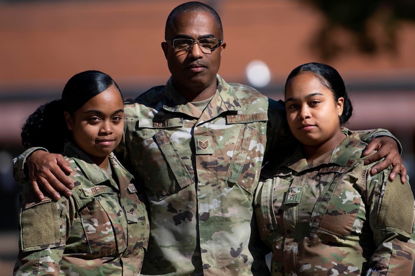 A man in uniform has his arms on the shoulders of two women in uniform.