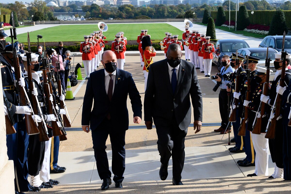 Two men walk up steps through a joint service honor guard.