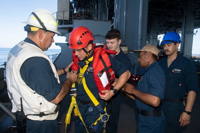 VICTORIA, Seychelles (Oct. 29, 2021) Deck Department assist Seaman Apprentice Ethan J. Dowden, second from left, in donning a harness to install the accommodation ladder aboard the Expeditionary Sea Base USS Hershel "Woody" Williams (ESB 4) as the ship pulls into port in Victoria, Seychelles, Oct. 29, 2021. Hershel "Woody" Williams is on a scheduled deployment in the U.S. Sixth Fleet area of operations in support of U.S. national security interests in Europe and Africa.