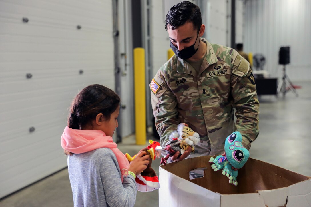 A soldier wearing a face mask gives an Afghan child a stuffed animal.
