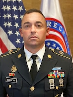 man in u.s. army uniform standing in front of two flags.