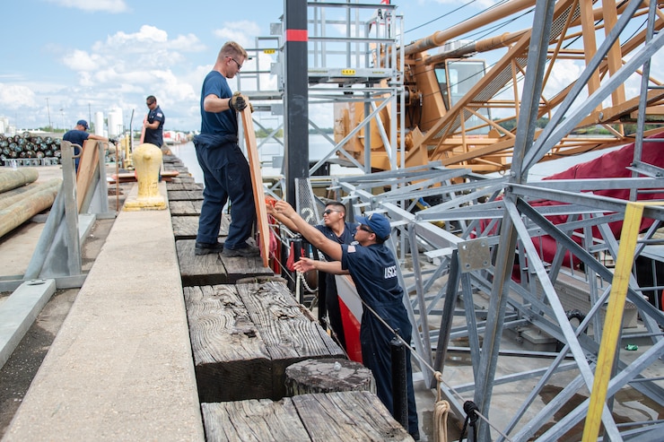 Petty Officer 3rd Class Peter Bessonoff hands a range marker board to Seaman Aurelio Rojas, and Seaman Jarrod Pell aboard the Coast Guard Cutter Axe in Morgan City, Louisiana, Sept. 20, 2021. The U.S. Coast Guard Cutter Axe (WLIC-75310) crew prepares to go underway to work on aids to navigation damaged by Hurricane Ida in the southern region of Louisiana. (U.S. Coast Guard photo by Petty Officer 3rd Class Vincent Moreno)