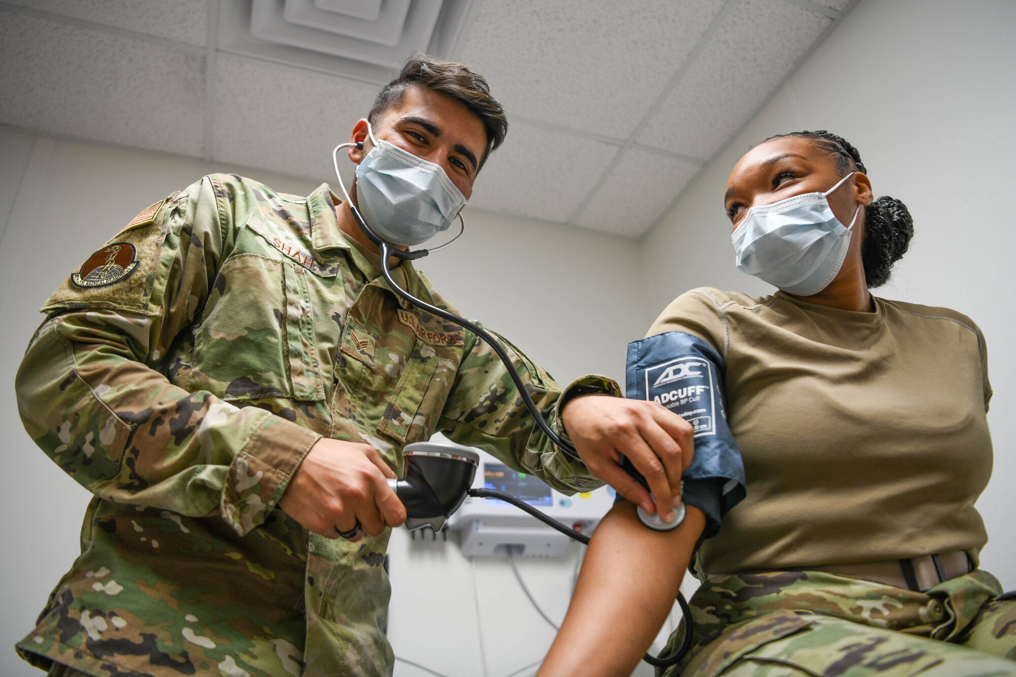 An Airman in uniform simulates taking a co-workers blood pressure.