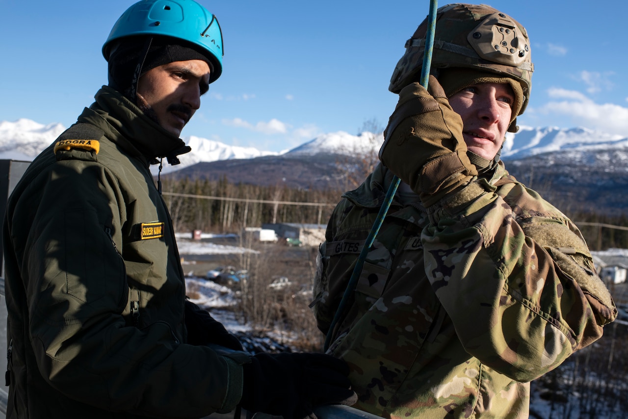 Two soldiers stand next to each other while one holds a rope.