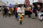 Group of adults stand outside of open car trunks ready to pass out candy.