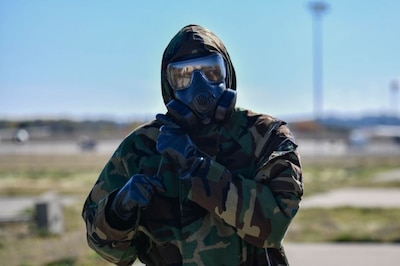 U.S. Air Force Airman from Team Fairchild tightens the draw string fastening on their Mission Oriented Protective Posture (MOPP) equipment during a large readiness exercise at Fairchild Air Force Base, Washington, Oct. 7, 2021. The scenario required Airmen to properly don their gear during a chemical, biological, radiological and nuclear attack (CBRN) scenario. (U.S. Air Force photo by Senior Airman Ryan Gomez)