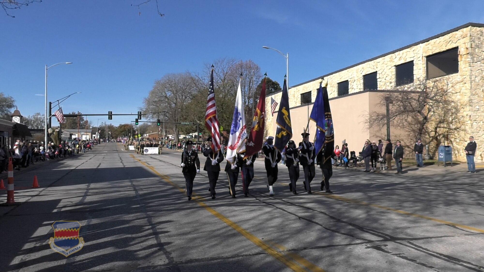 Air Force uniformed service members carry flags in a color guard formation down a street.